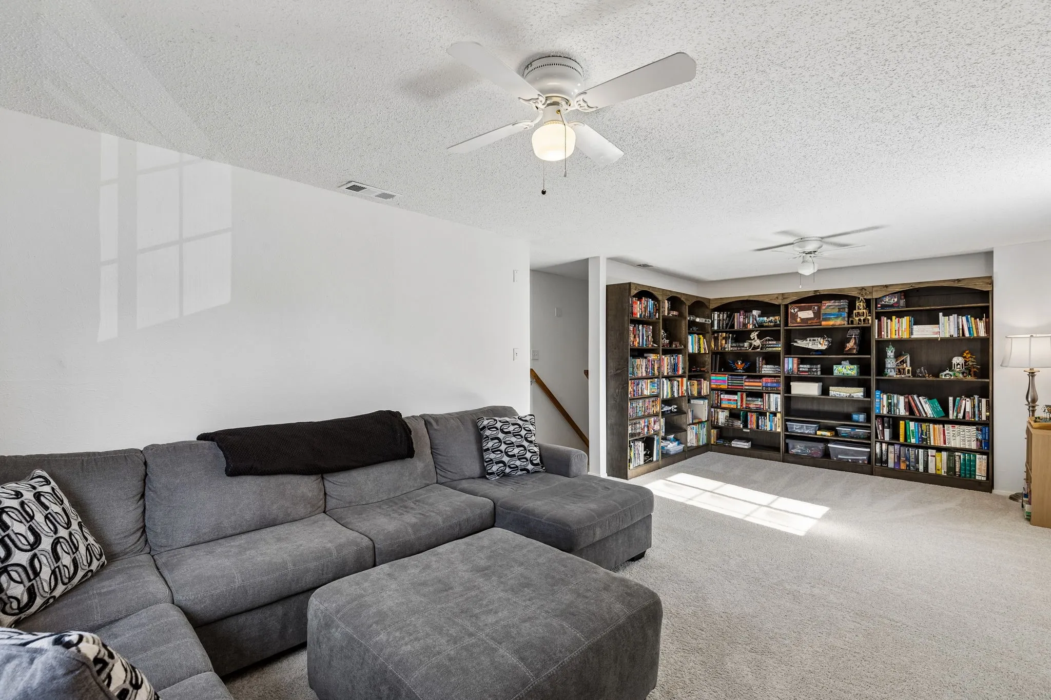 Built-in full-wall shelving, dual ceiling fans, and neutral wall-to-wall carpeting