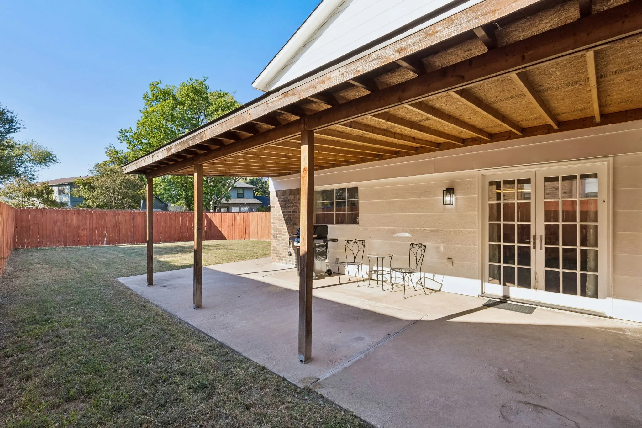 Covered patio featuring a concrete slab and exposed wood beam ceiling, paired with glass-paned French doors and a fenced backyard