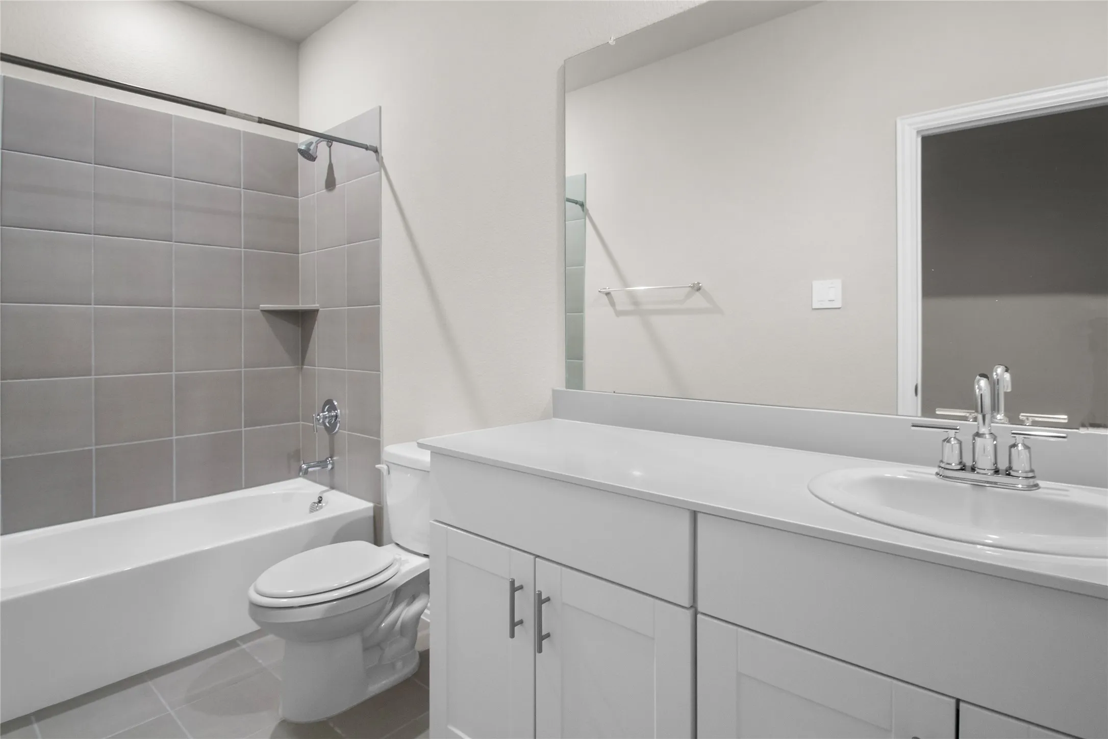 Bathroom featuring a white vanity with a composite countertop, an integrated sink, a large wall-mounted mirror, and a tub-shower combination with oversized grey ceramic tile surround