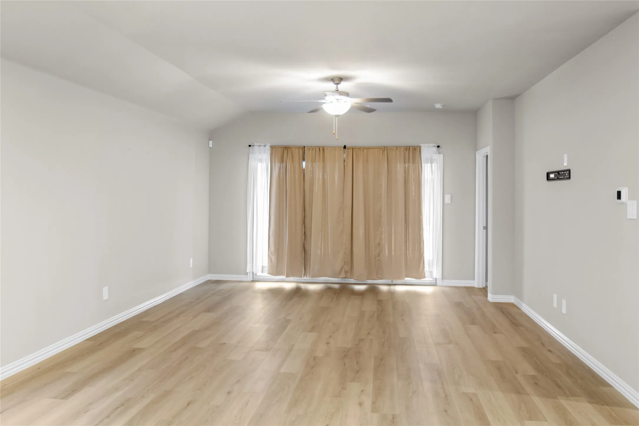 Vaulted ceilings featuring a central ceiling fan, wood-finish flooring, and glass sliding doors