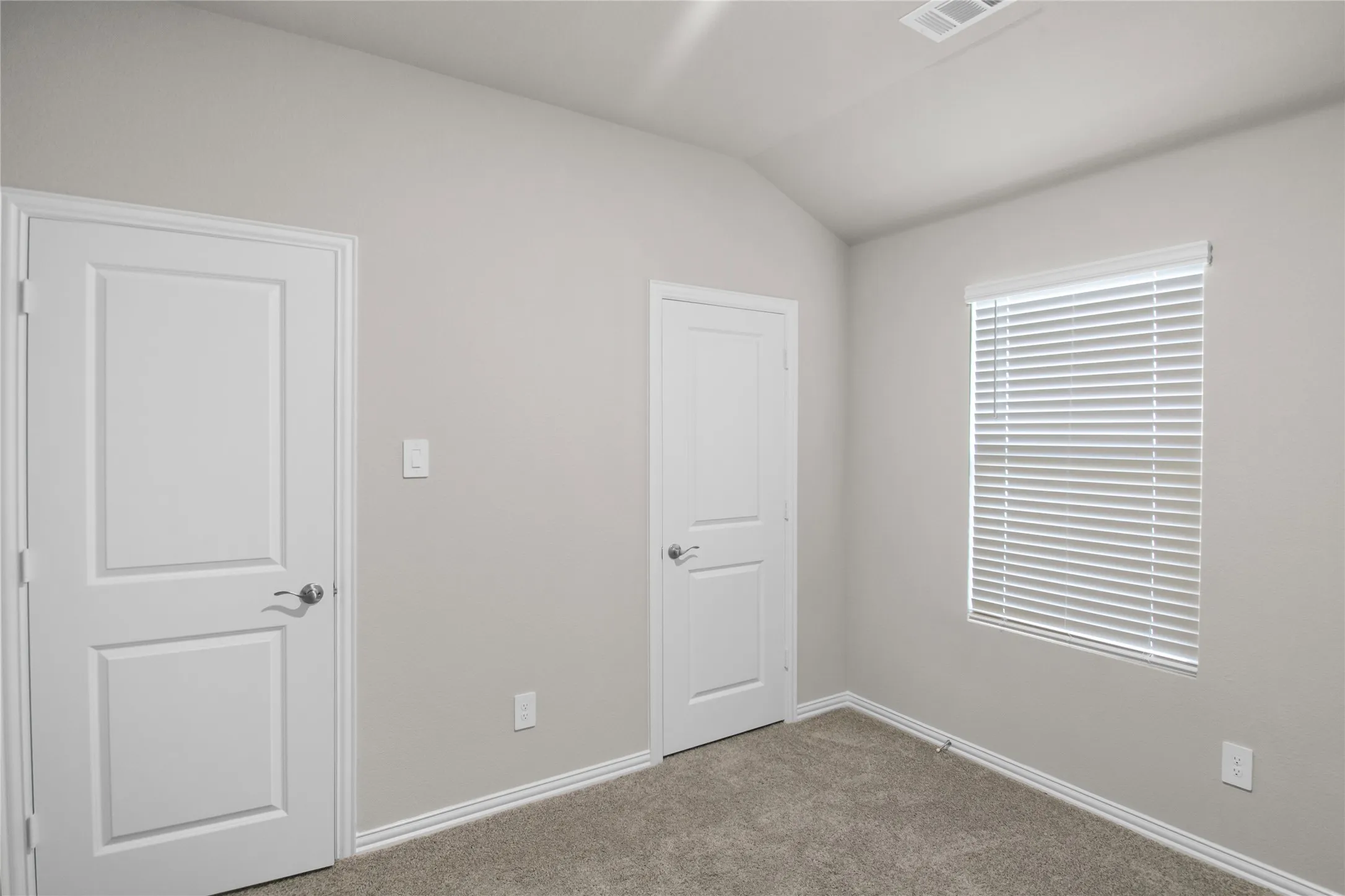 Vaulted ceiling, neutral wall tones, interior two-panel doors, and horizontal slat window blinds
