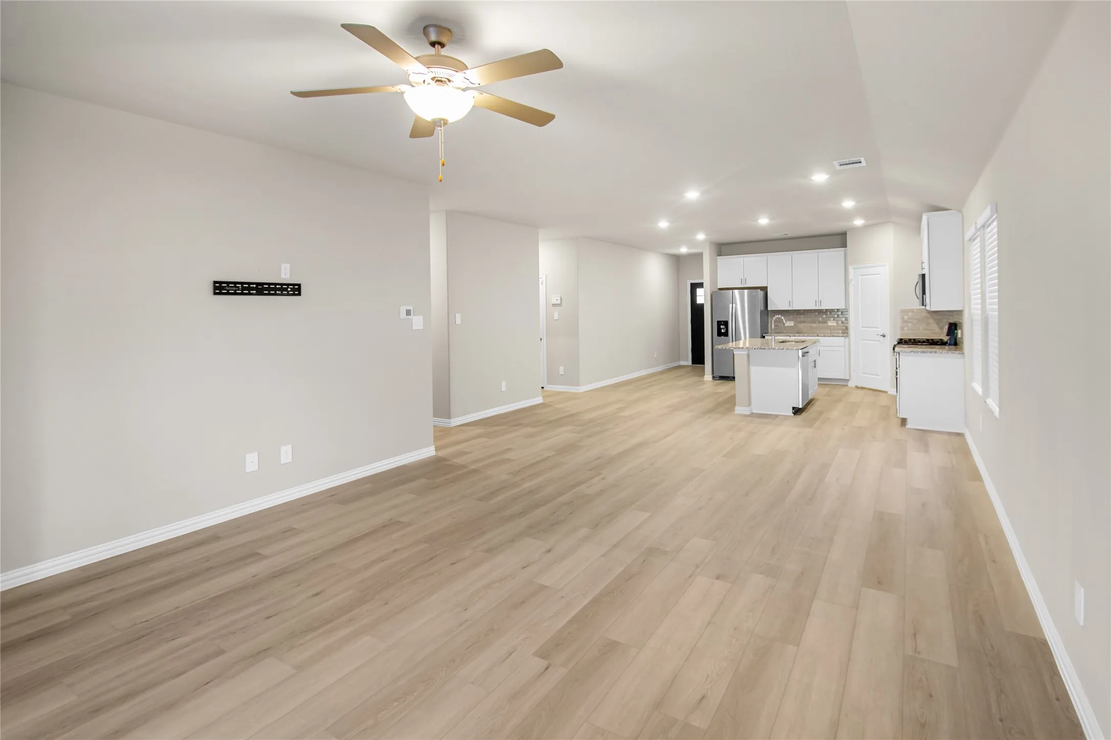 Open-concept interior featuring wood-finish flooring, recessed lighting, a ceiling fan, and a kitchen equipped with white cabinetry and a center island
