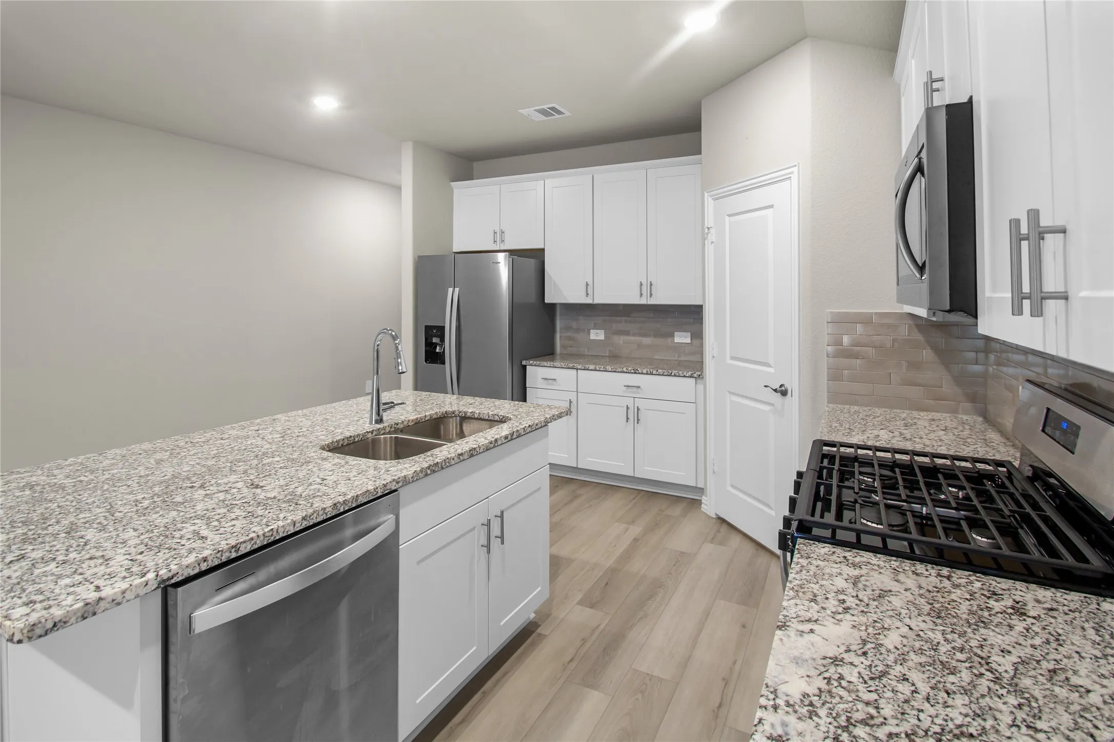 Kitchen featuring white shaker-style cabinetry, stone-finish countertops, subway tile backsplash, stainless steel appliances, and wood-finish flooring