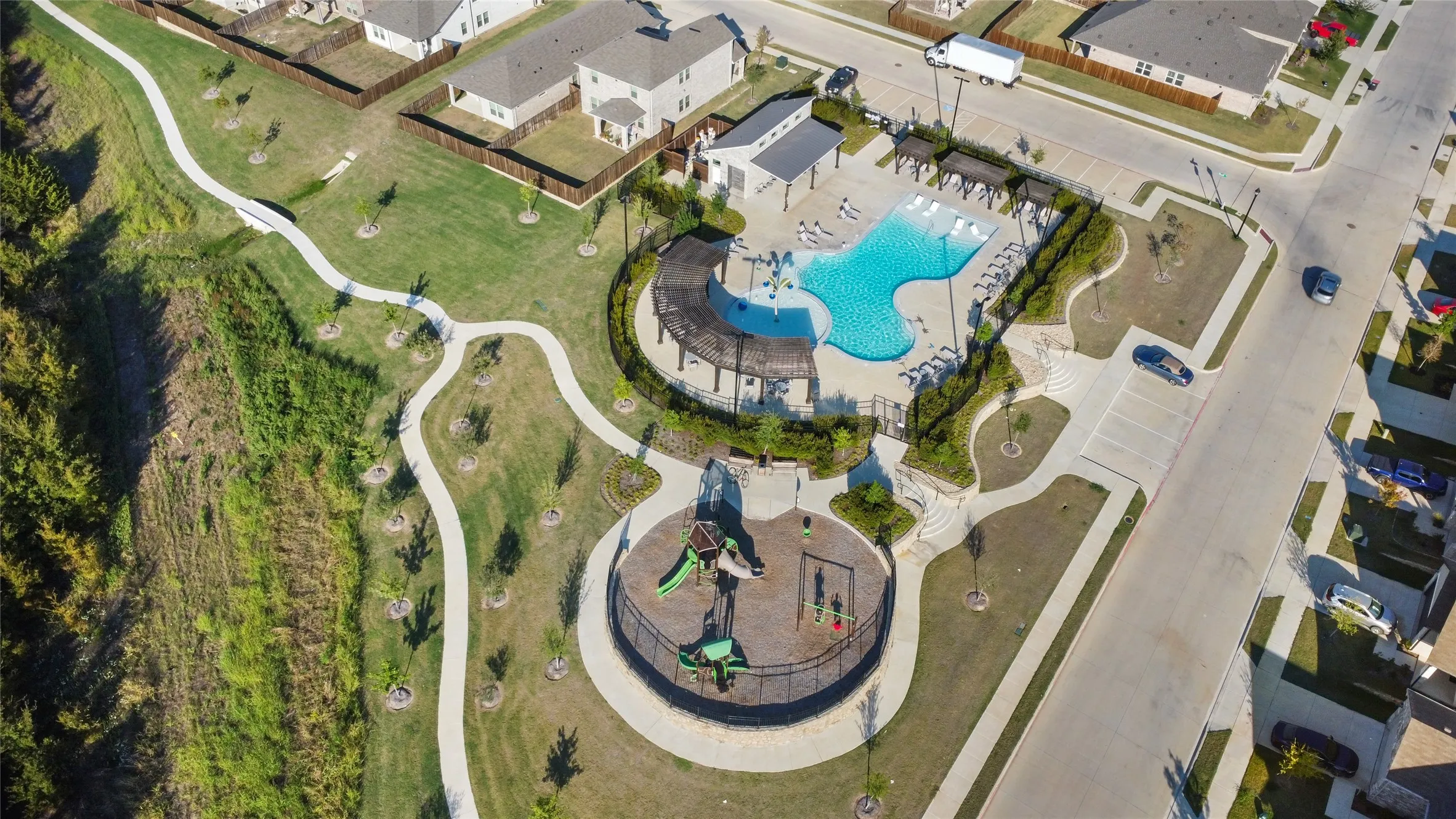 Community recreational area featuring a swimming pool, pergola-covered lounge space, playground, and concrete walking paths