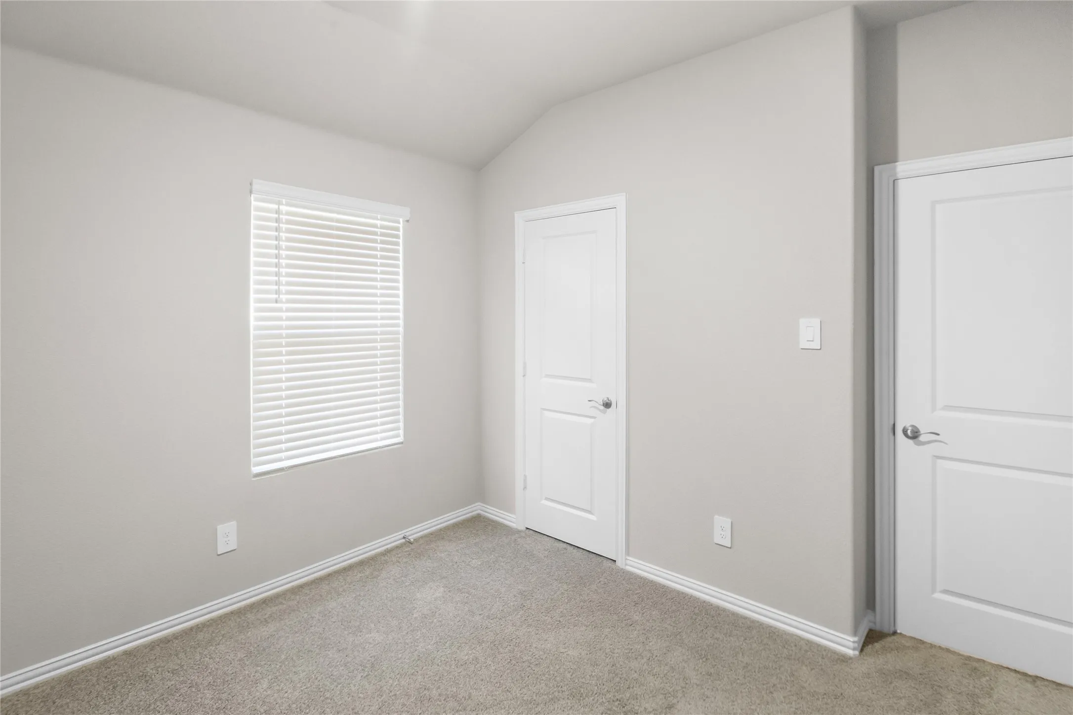 Neutral interior featuring high vaulted ceilings, wall-to-wall carpeting, two panel-style doors, and a window with horizontal blinds