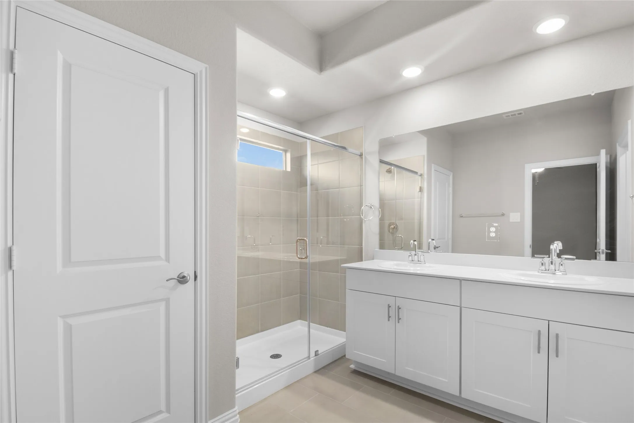 Double vanity with white cabinetry, solid-surface countertops, dual undermount sinks, frameless glass-enclosed shower with tiled walls, and recessed lighting