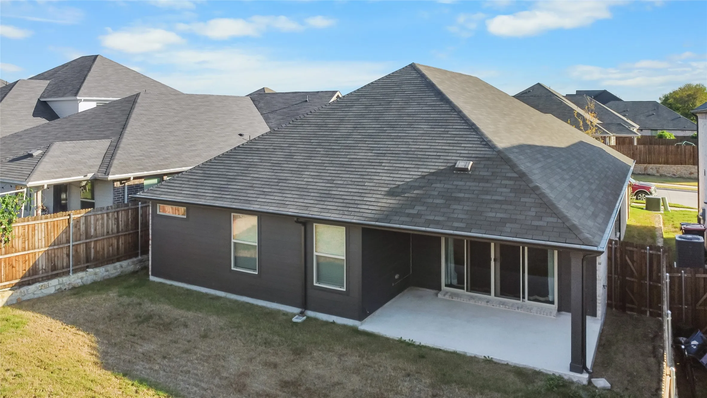 Rear elevation featuring a covered concrete patio, dark-toned exterior siding, a shingled roof, and perimeter wood fencing