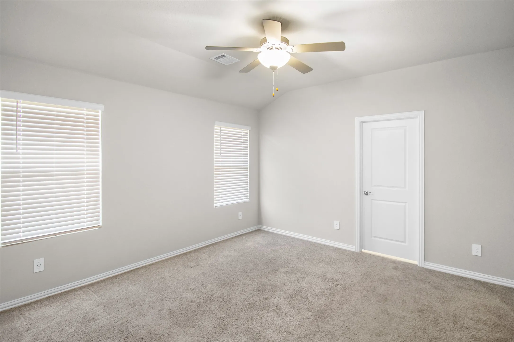 Vaulted ceilings featuring a centrally mounted ceiling fan with integrated lighting, neutral wall-to-wall carpeting, and two windows equipped with horizontal blinds