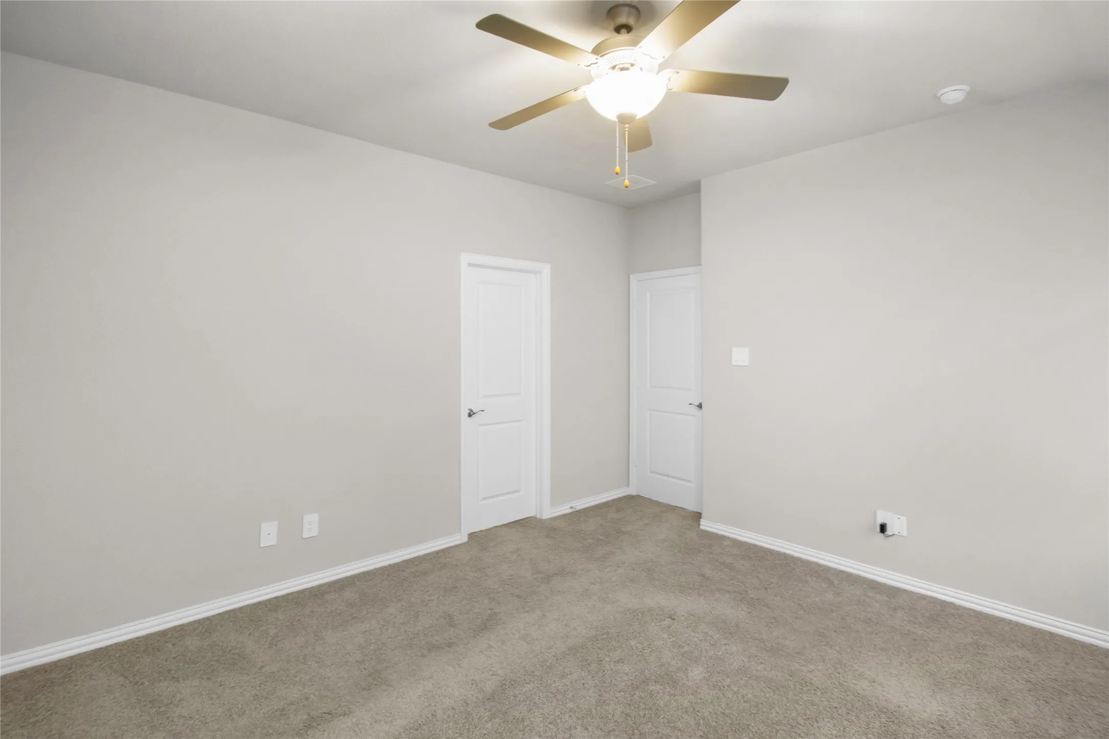 Neutral-toned interior space featuring plush wall-to-wall carpeting, two interior doors, and a ceiling fan with integrated lighting
