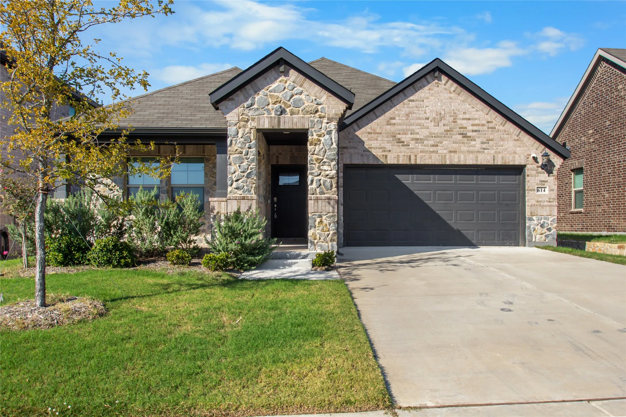 Single-story exterior featuring a brick and stone facade, dual-gabled roofline, concrete driveway, and attached two-car garage