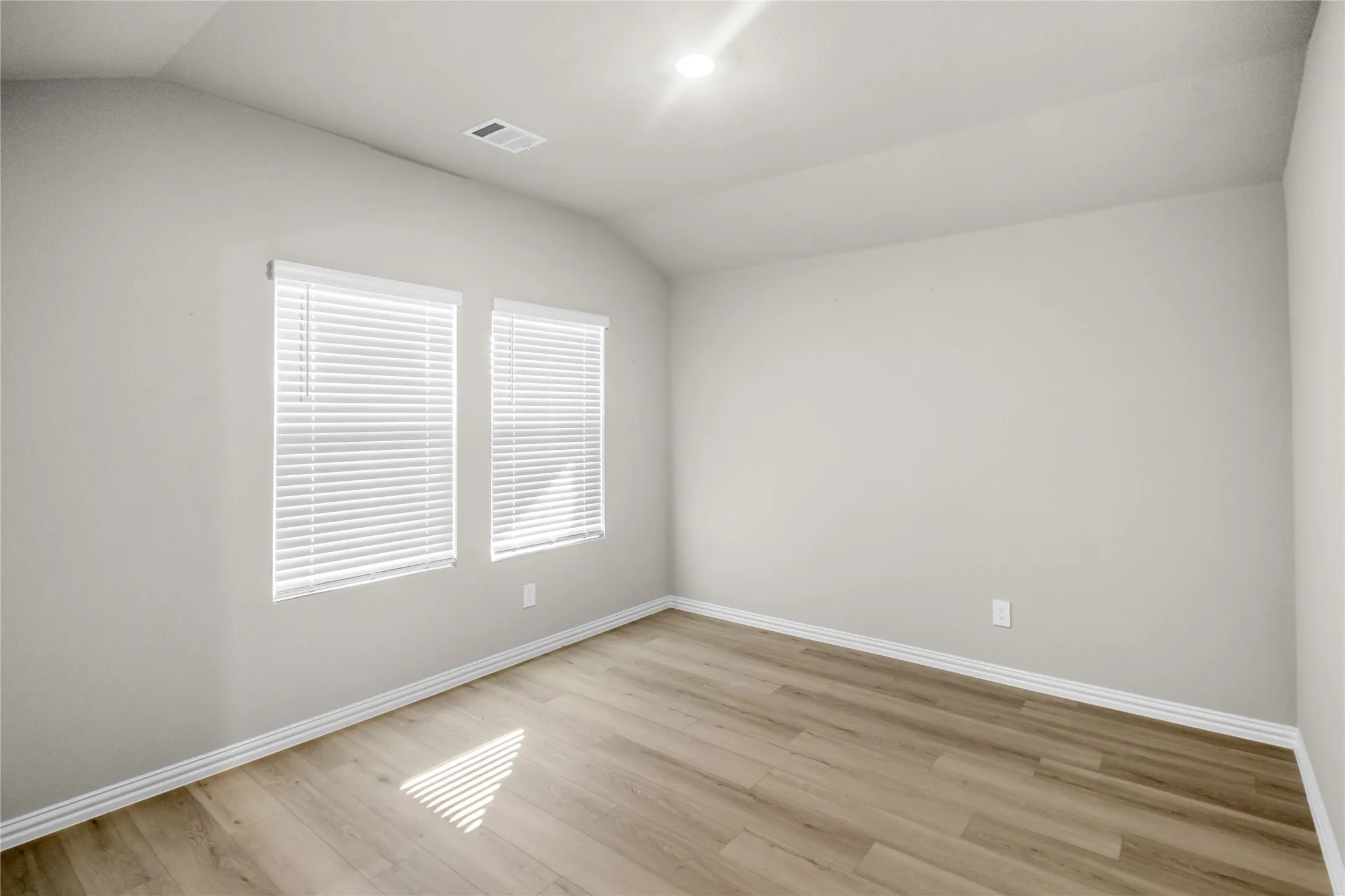 Vaulted ceiling featuring neutral wall paint, wood-finish flooring, and dual windows with fitted blinds