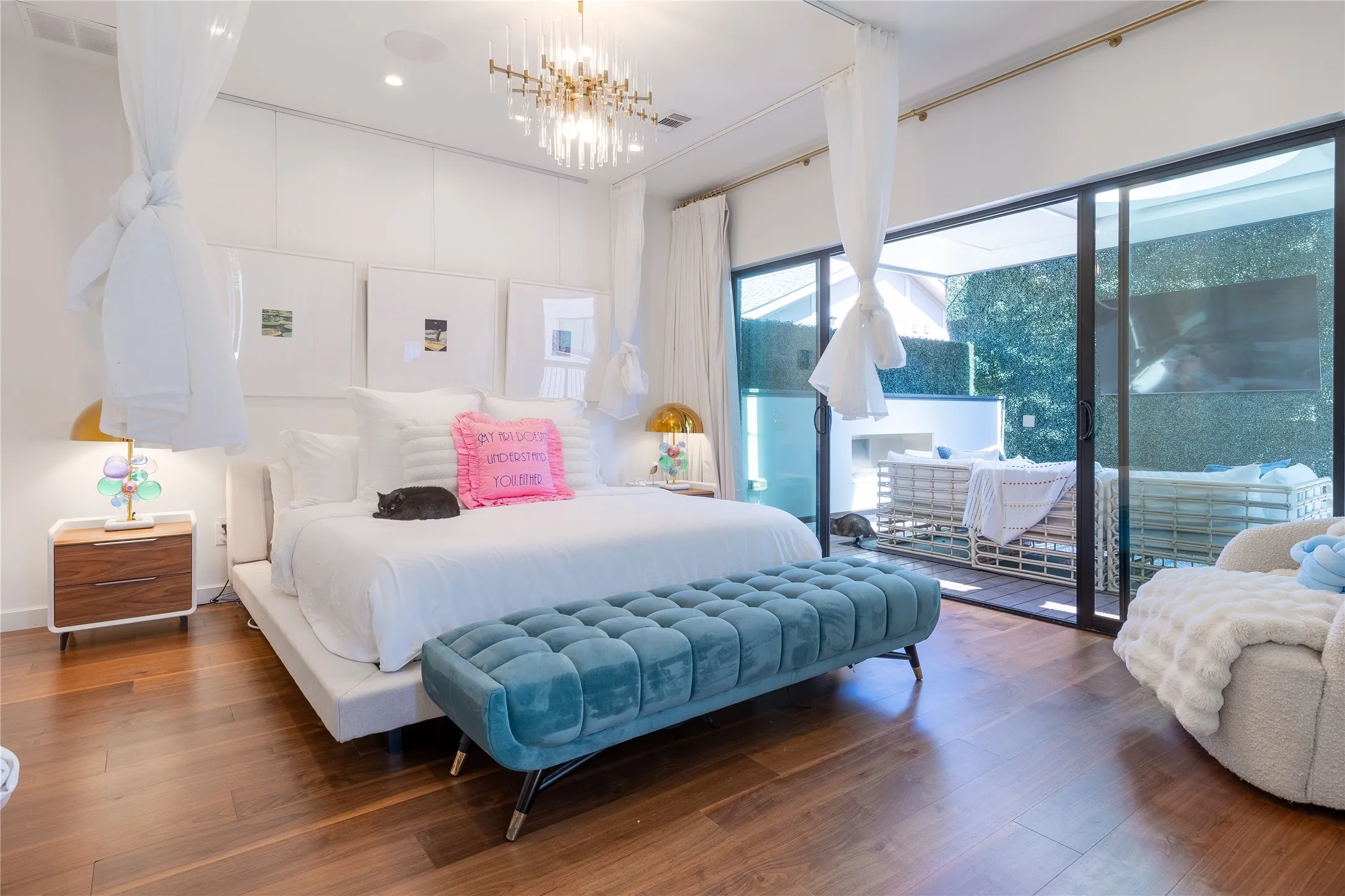 Large primary bedroom opens up to a cozy resort-style covered balcony with a fireplace, a wall of green, and a view down to the beautiful pool area.