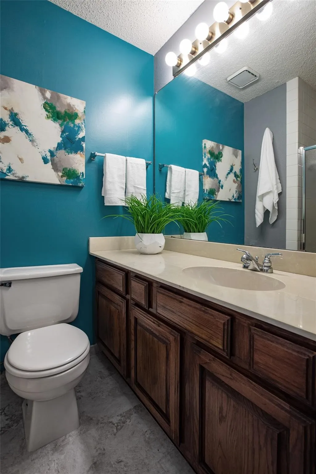 Bathroom featuring a stone-composite countertop, dark wood-finish cabinetry, an oval integrated sink, a full-width vanity mirror, and an eight-bulb Hollywood-style light fixture