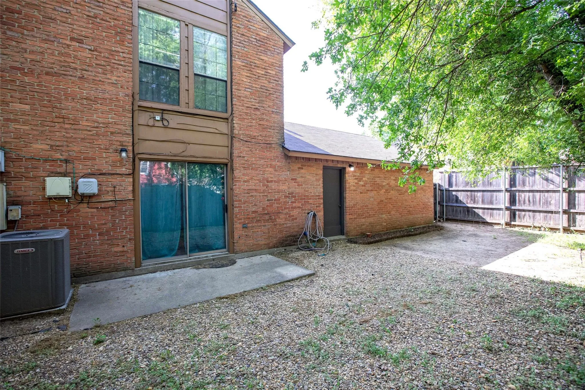 Exterior featuring brick facade, concrete patio, sliding glass door, and perimeter wood privacy fencing
