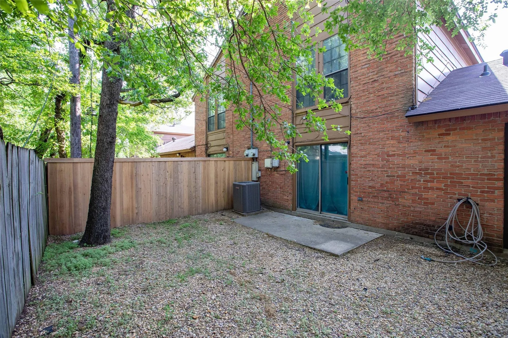 Brick exterior with sliding glass doors, concrete patio, and a wood privacy fence