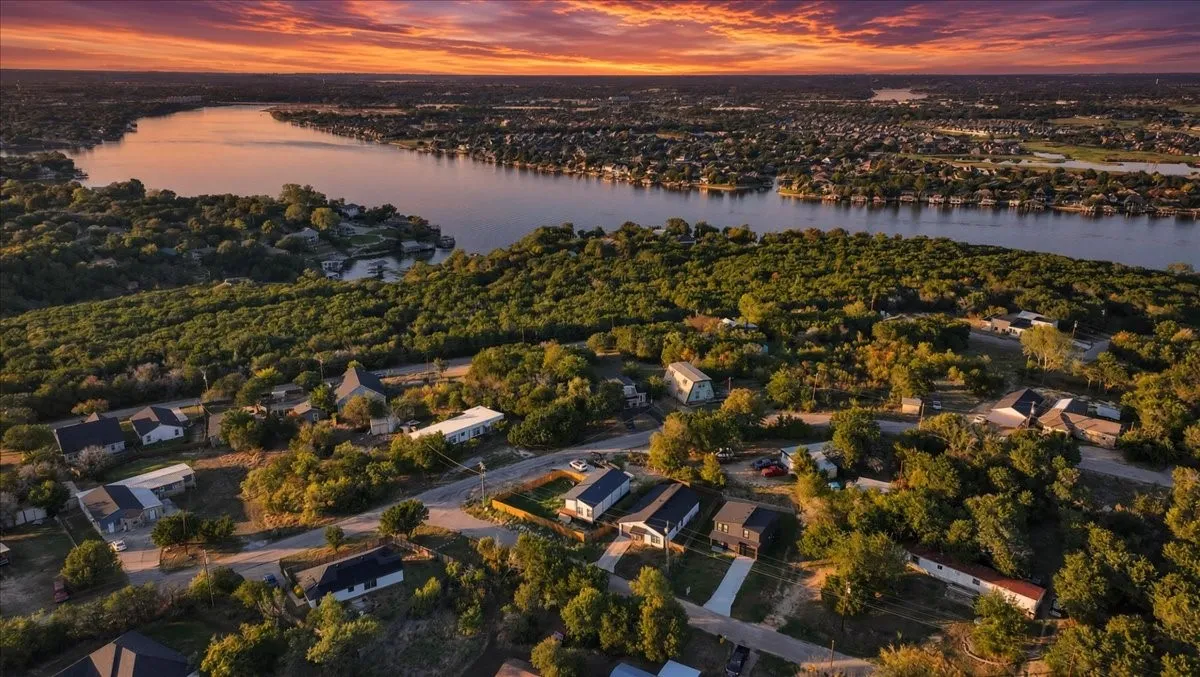 Aerial perspective featuring a waterfront location, mature canopy of trees, and sunset horizon