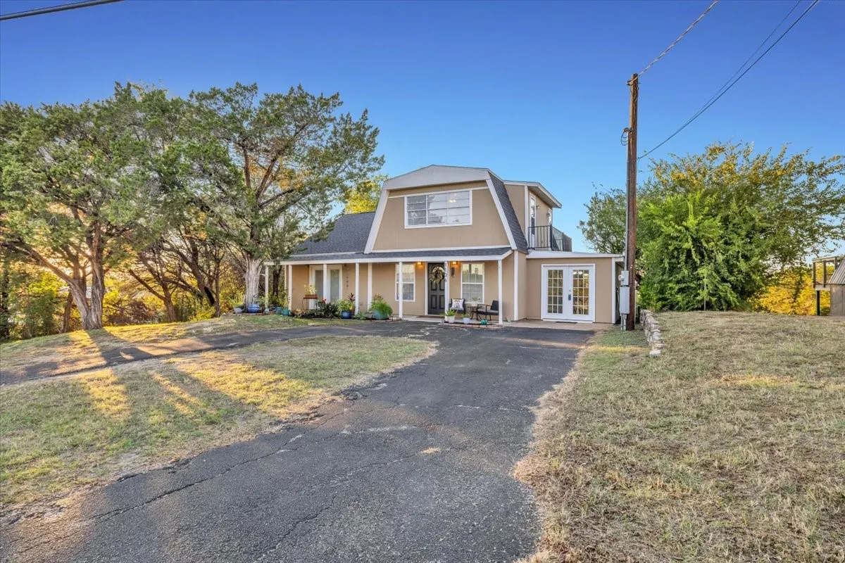 Gambrel-style residence featuring a covered front porch, dual-entry French doors, and a paved driveway