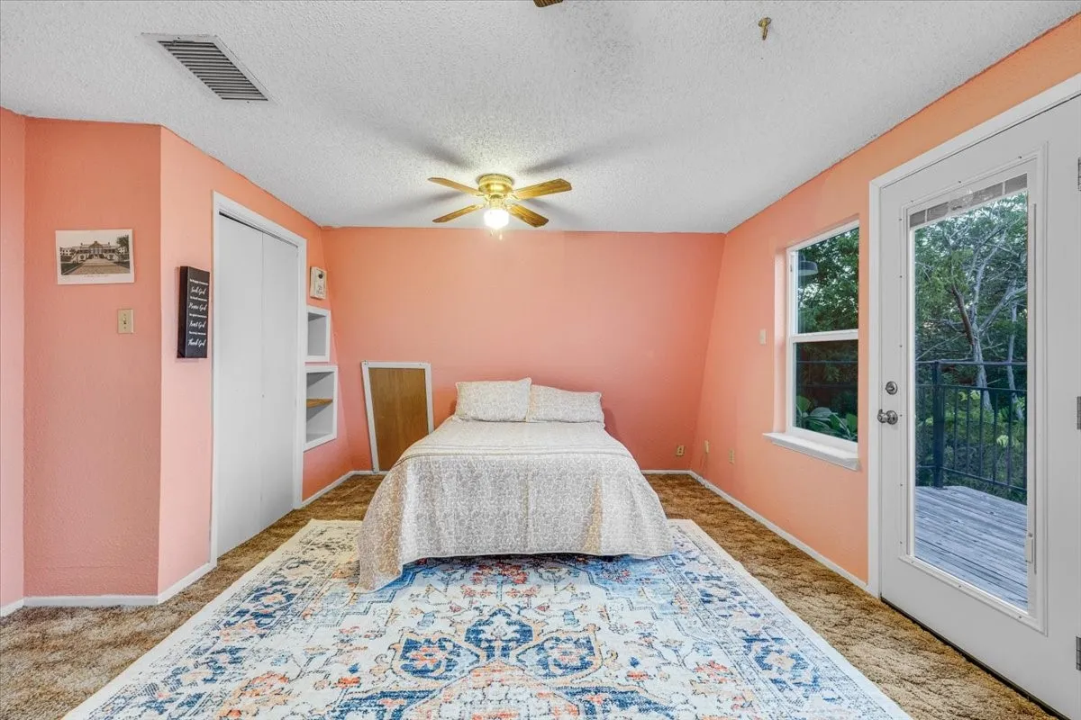 Room with carpeted flooring, vaulted ceiling, built-in recessed shelving, central ceiling fan, and a glass-paneled exterior door