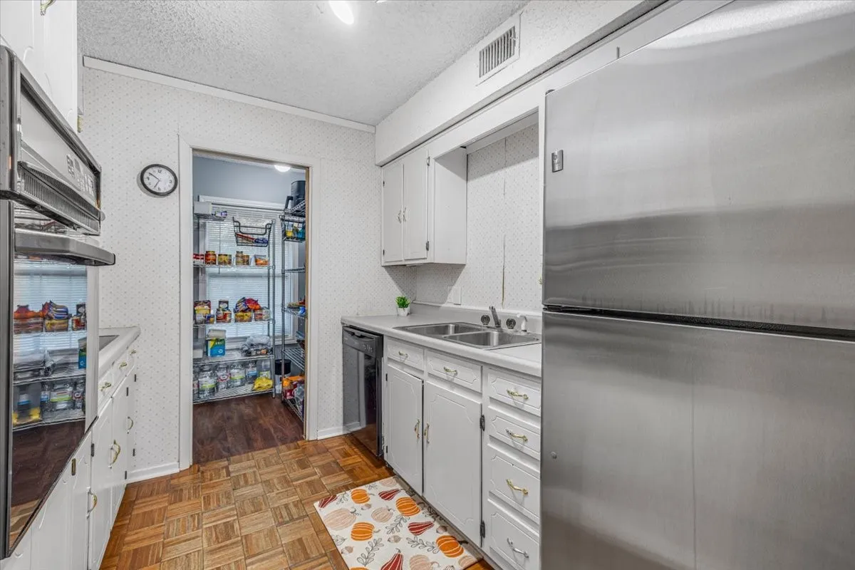 Kitchen featuring stainless steel refrigerator, built-in wall oven, dual-basin stainless steel sink, wood-finish parquet flooring, and white cabinetry