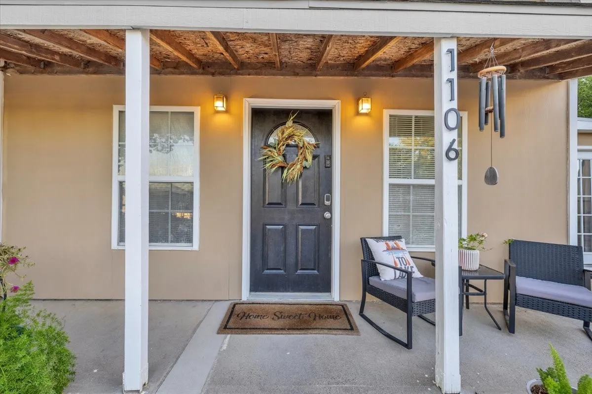Covered front porch featuring a concrete foundation, dual exterior wall-mounted sconces, and a paneled entry door with an arched glass inset