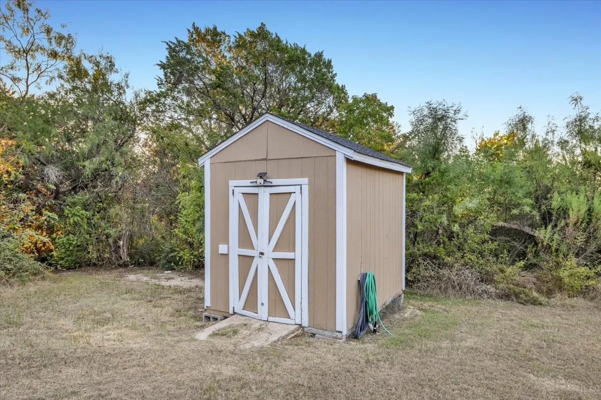 Storage shed featuring wood-panel siding, double doors with X-bracing, a shingled roof, and a concrete entry pad