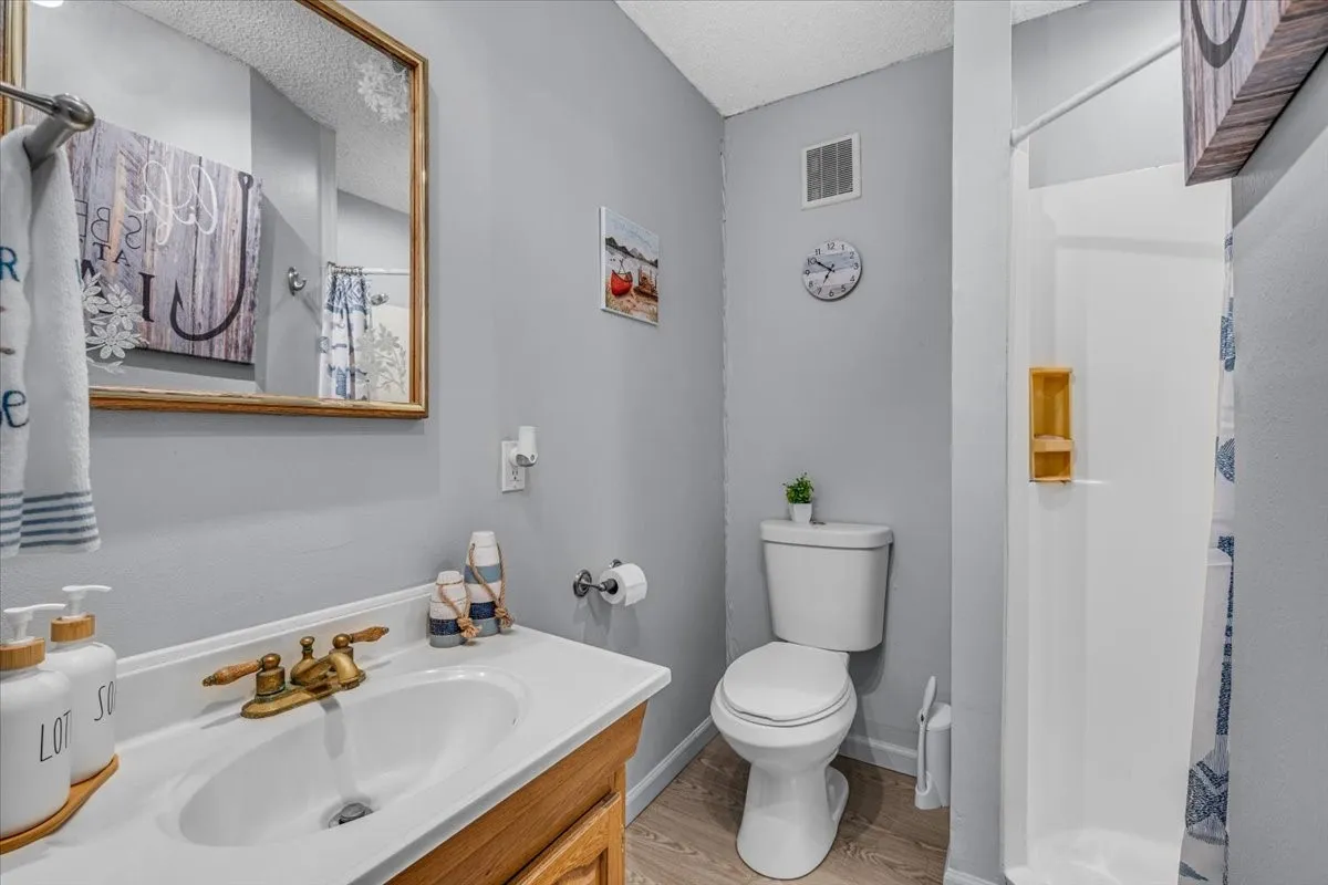 Bathroom featuring a wood-finish vanity with an integrated white sink, metallic faucet hardware, wood-finish flooring, and a walk-in shower surround