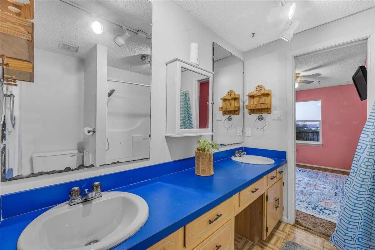 Bathroom vanity featuring an extended solid-surface countertop, dual integrated oval sinks, light-wood cabinetry, a wall-mounted mirrored medicine cabinet, and large-format wall mirrors