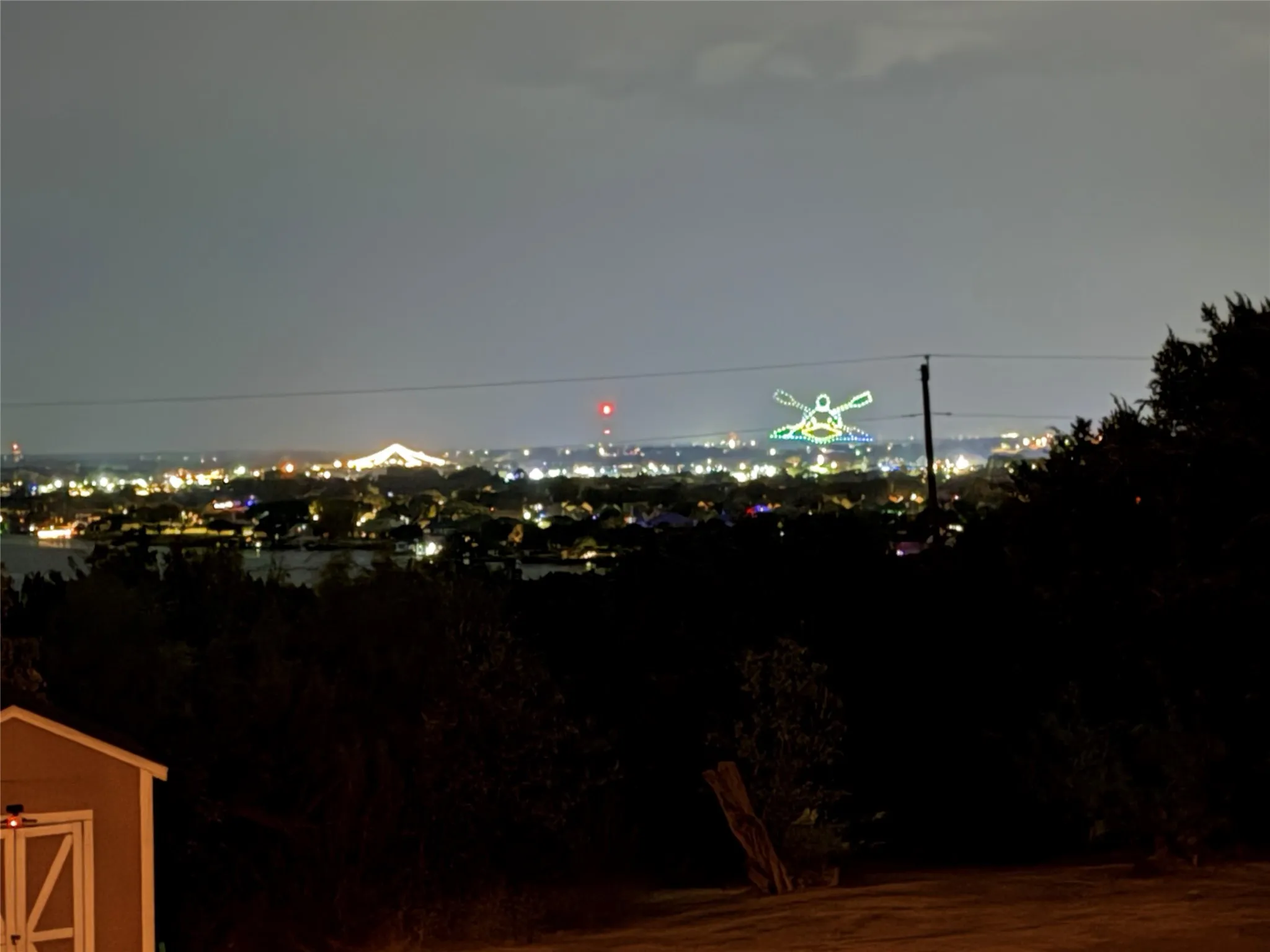 Elevated nocturnal scenery featuring expansive city lights, distant illuminated structures, and a wooden storage structure