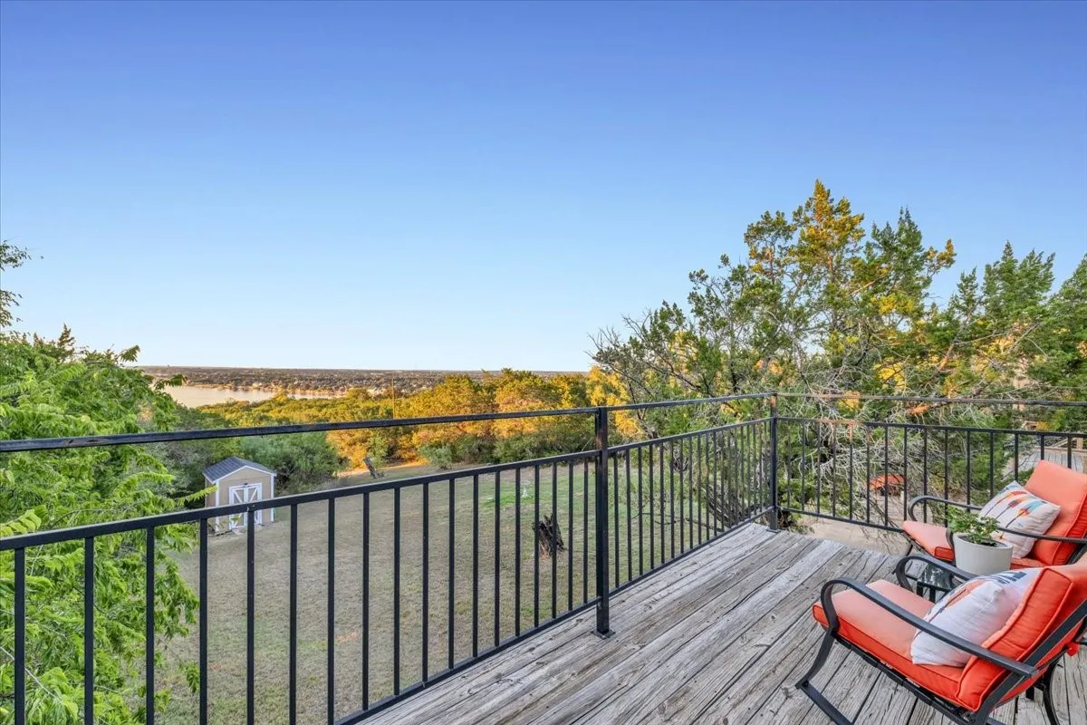 Elevated wooden deck with black metal railing overlooking a landscape featuring mature trees and a detached storage shed