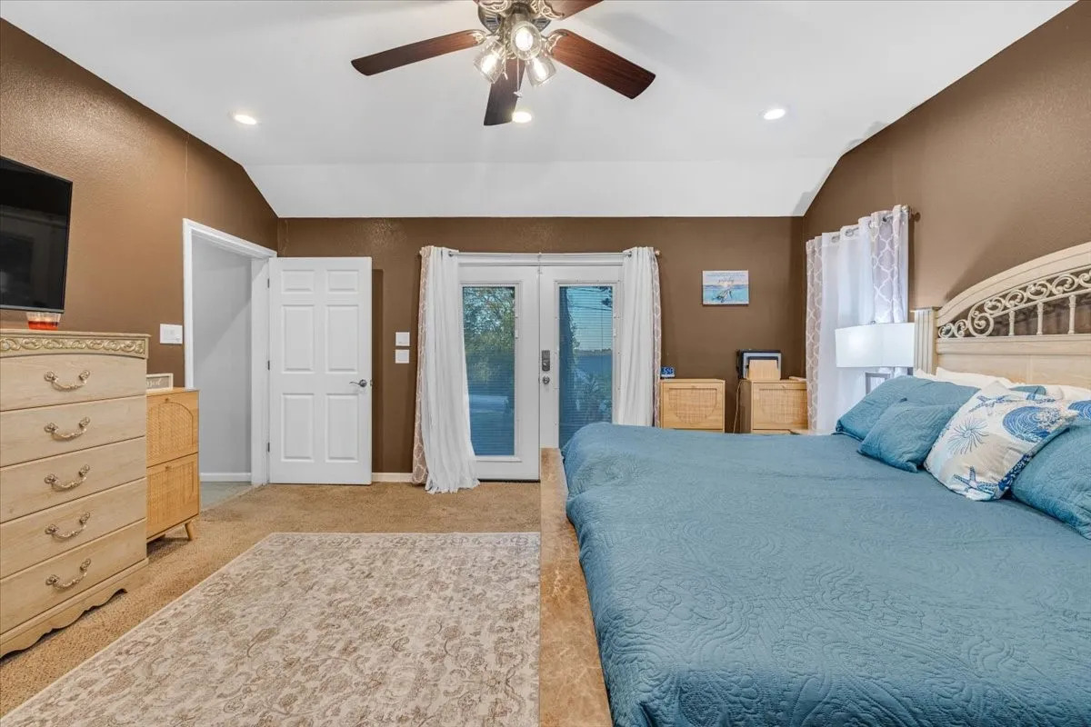Vaulted ceiling with a central multi-blade ceiling fan and recessed lighting, paired with double glass-panel doors providing external access