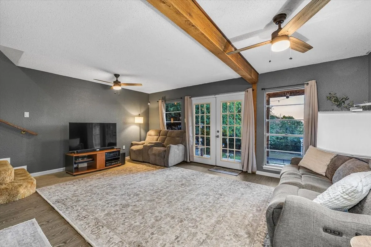 Living area featuring exposed wood ceiling beams, wood-finish flooring, dual ceiling fans, and French doors providing exterior access
