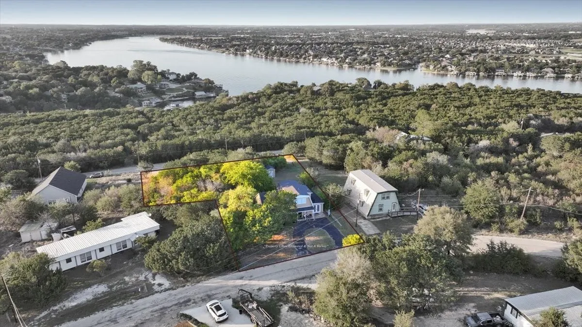 Aerial perspective of a property featuring mature trees, paved driveway, and proximity to a large body of water