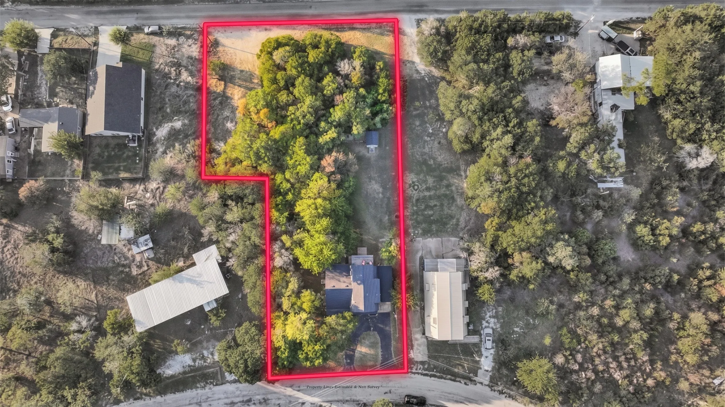 Aerial perspective of a multi-acre property featuring mature tree cover, a paved driveway, and established landscape