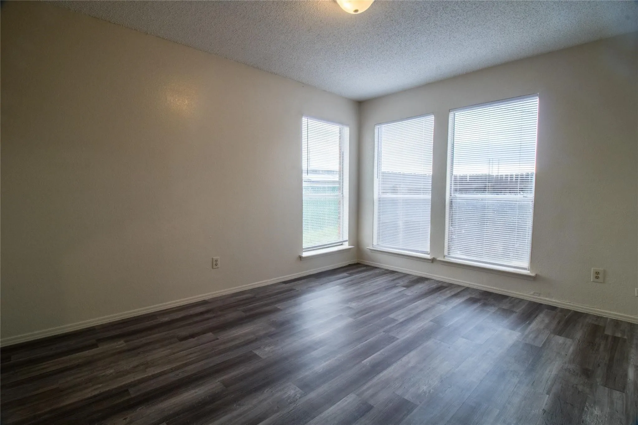 Room featuring wood-finish flooring, neutral wall tones, and three windows with installed blinds
