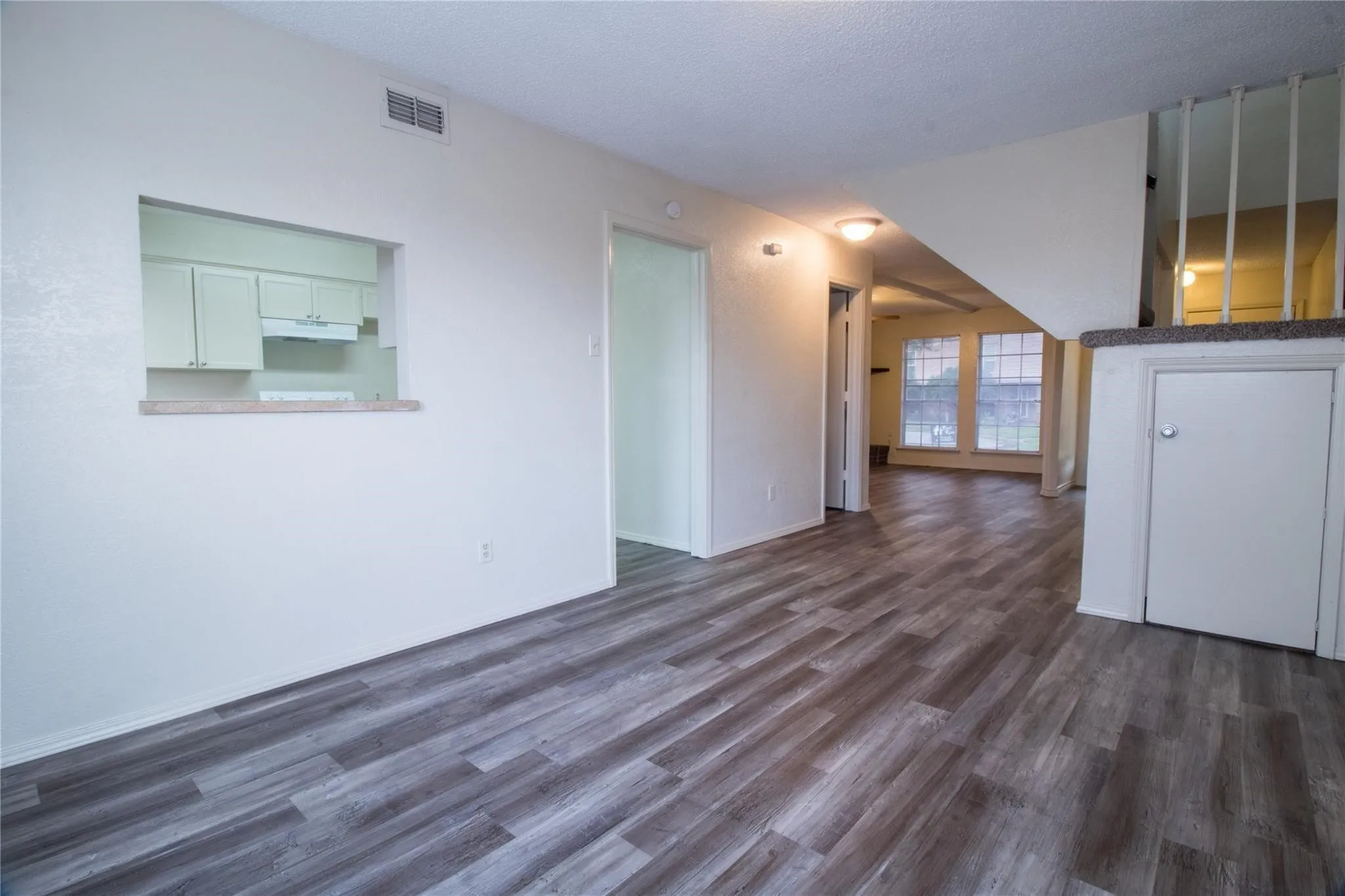 Interior featuring wood-finish flooring, a kitchen pass-through window, and a built-in storage cabinet with a staircase balustrade