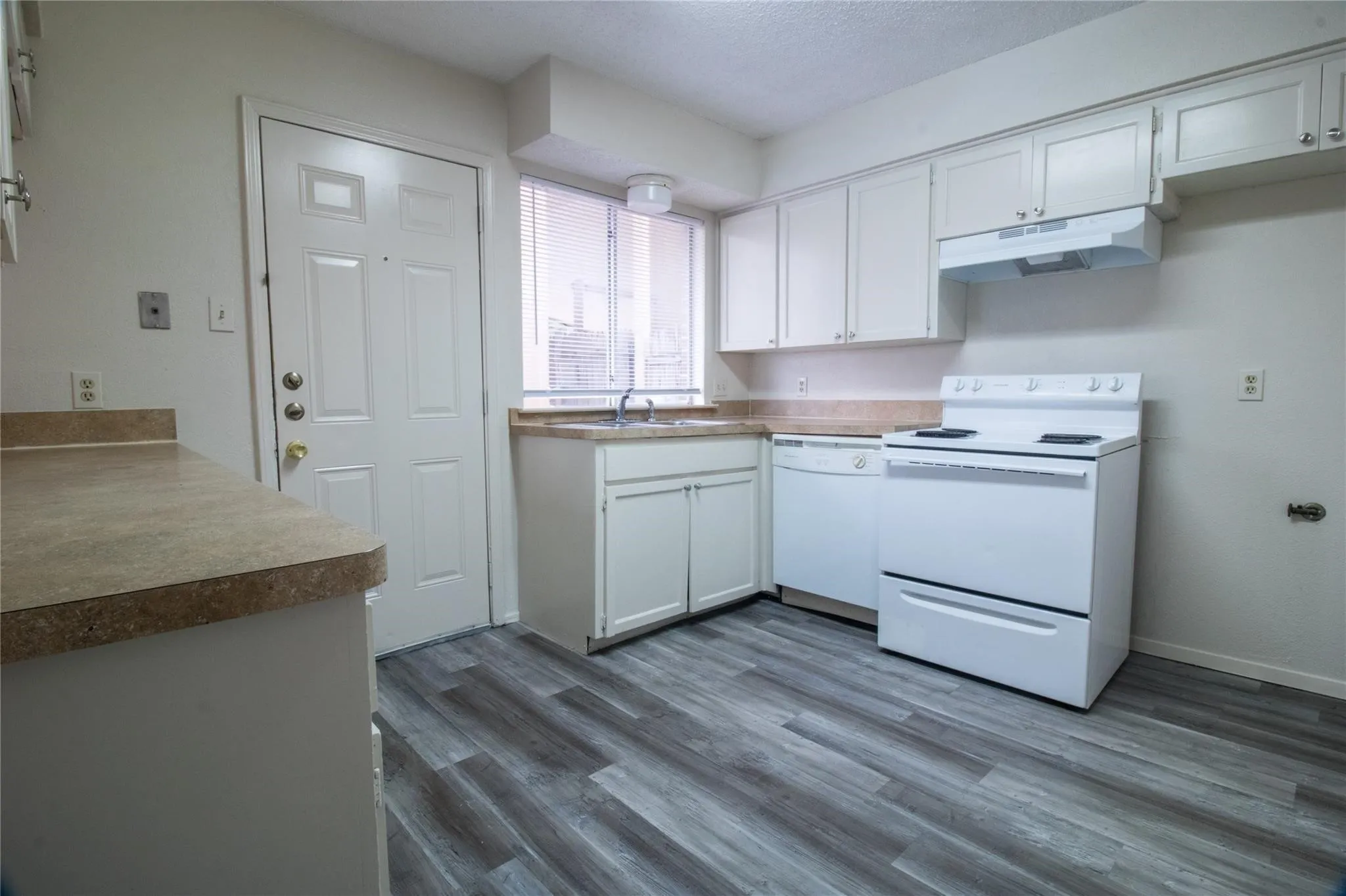 Kitchen featuring white cabinetry, wood-finish flooring, a stainless steel sink with a dual-handle faucet, and white appliances
