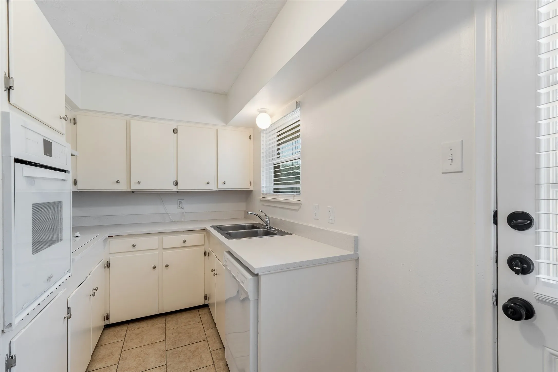 Kitchen featuring white cabinetry, solid-surface countertops, dual-basin stainless steel sink, built-in wall oven, and ceramic tile flooring