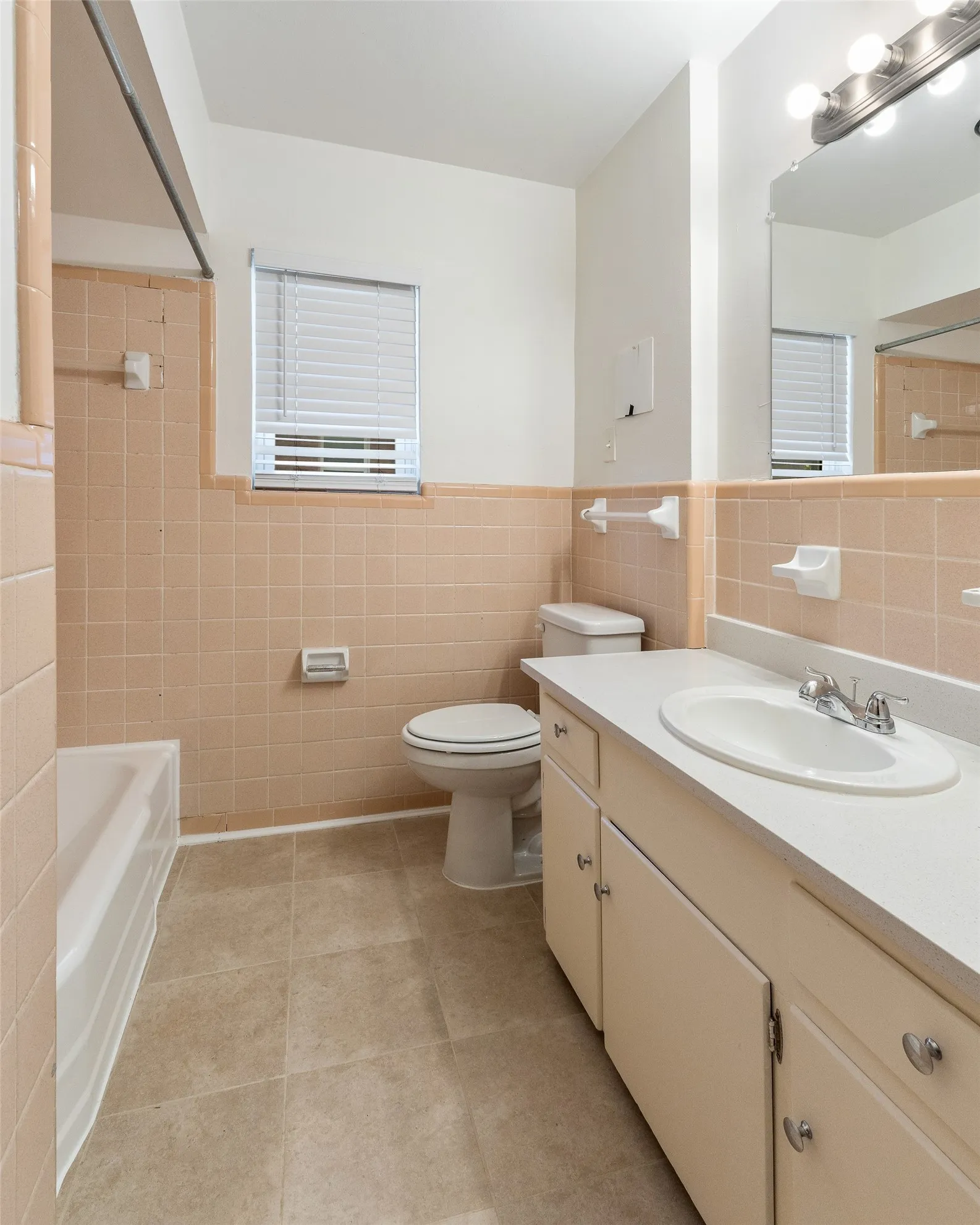 Bathroom featuring ceramic tile wall surrounds, a built-in vanity cabinet with a solid surface countertop, an integrated oval sink, and a multi-light fixture