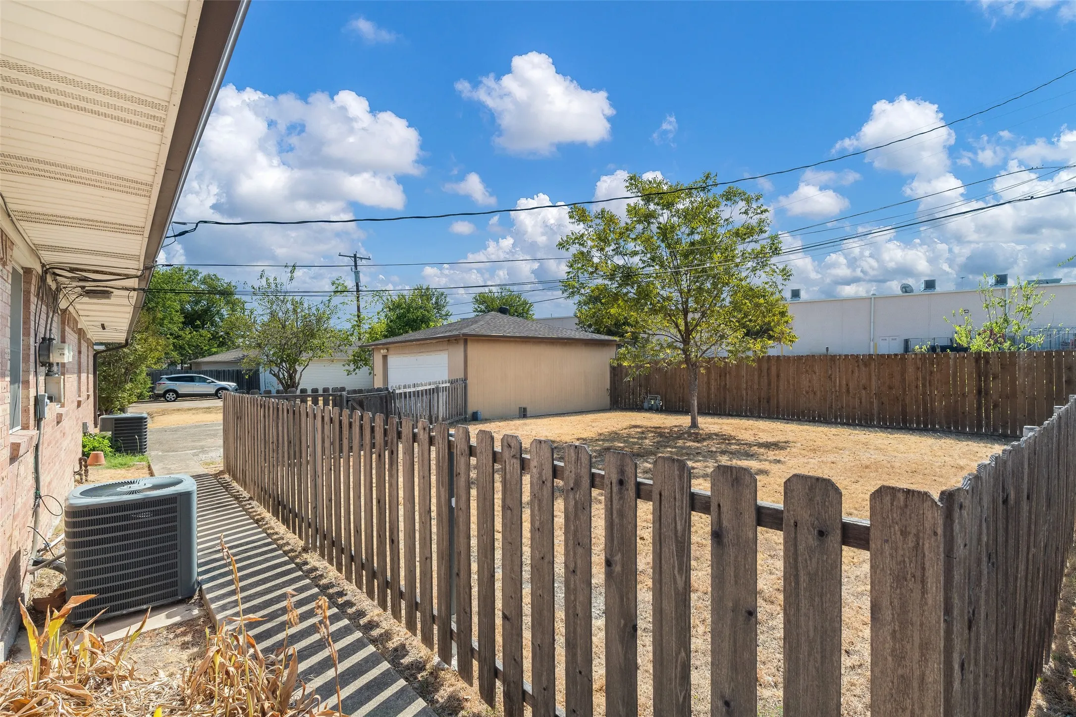 Fenced backyard featuring a detached garage, mature tree, and exterior central air conditioning unit