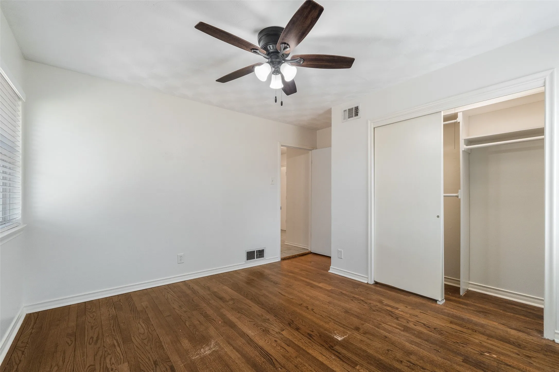 Wood-finish flooring, ceiling fan with integrated lighting, and closet with sliding doors