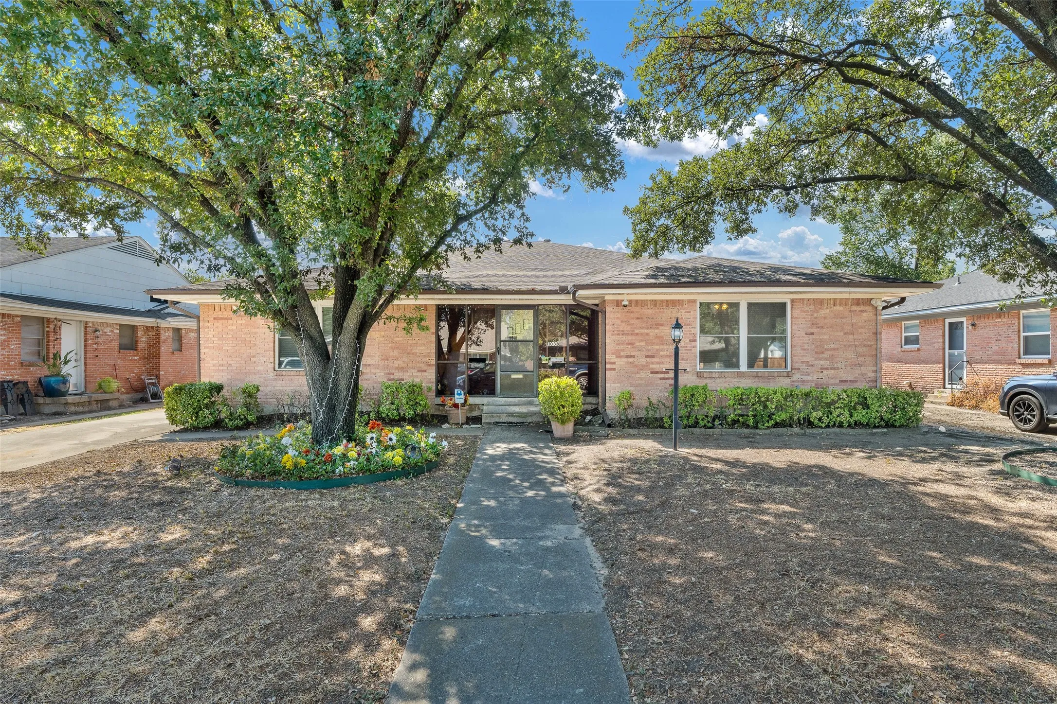 Single-story brick exterior featuring a covered front entryway, concrete walkway, and mature trees