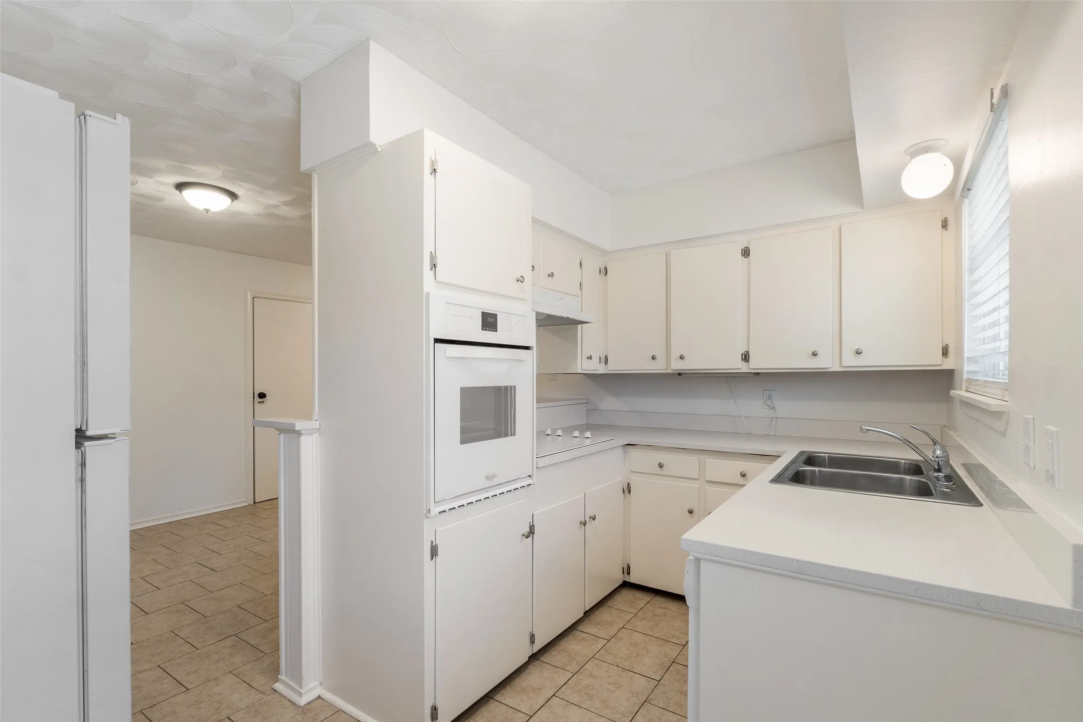 Kitchen featuring solid-surface countertops, dual-basin stainless steel sink, built-in wall oven, flush-mount lighting, and tile flooring
