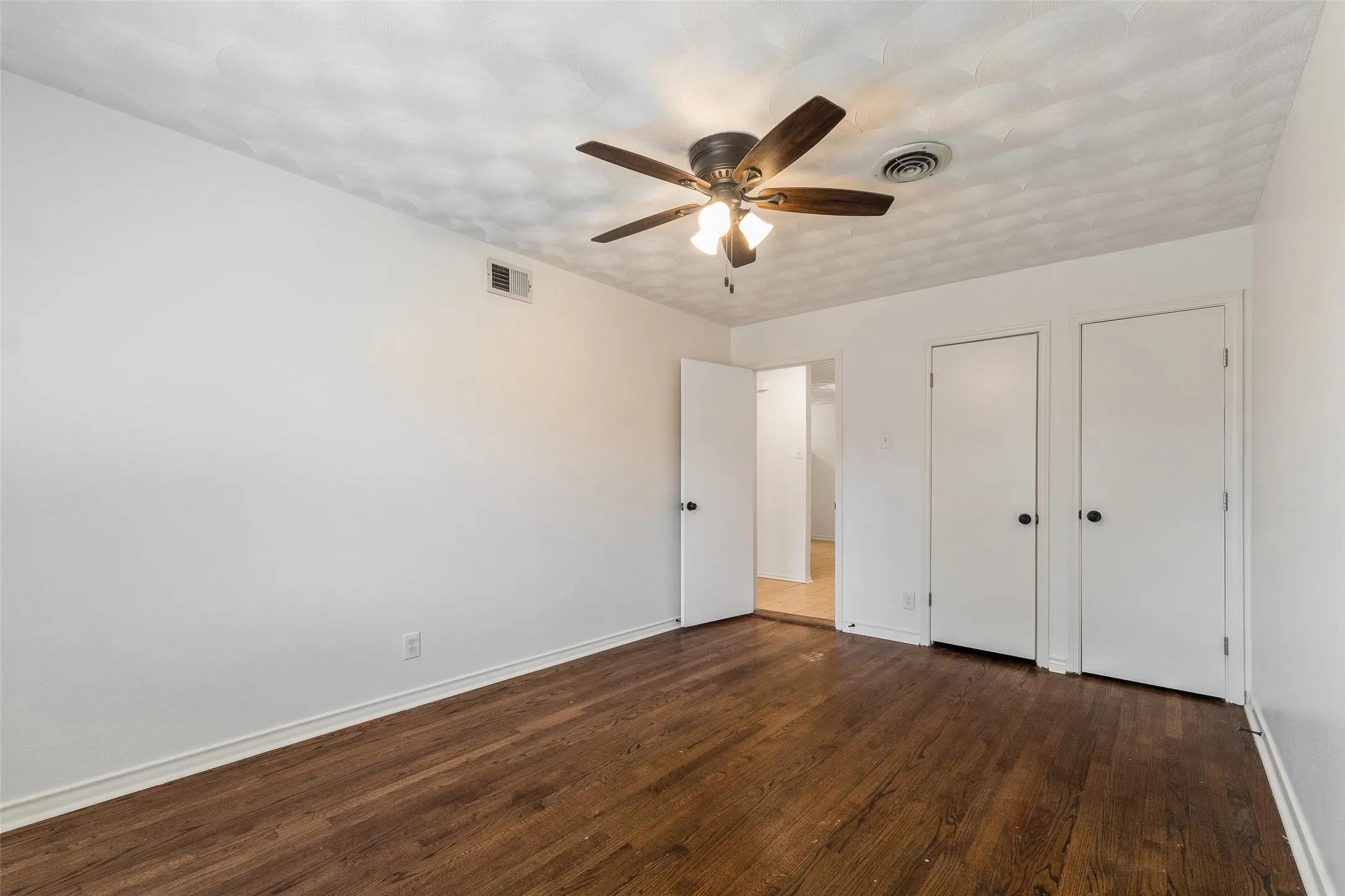 Room featuring wood-finish flooring, textured ceiling, central ceiling fan with integrated lighting, and dual built-in closets