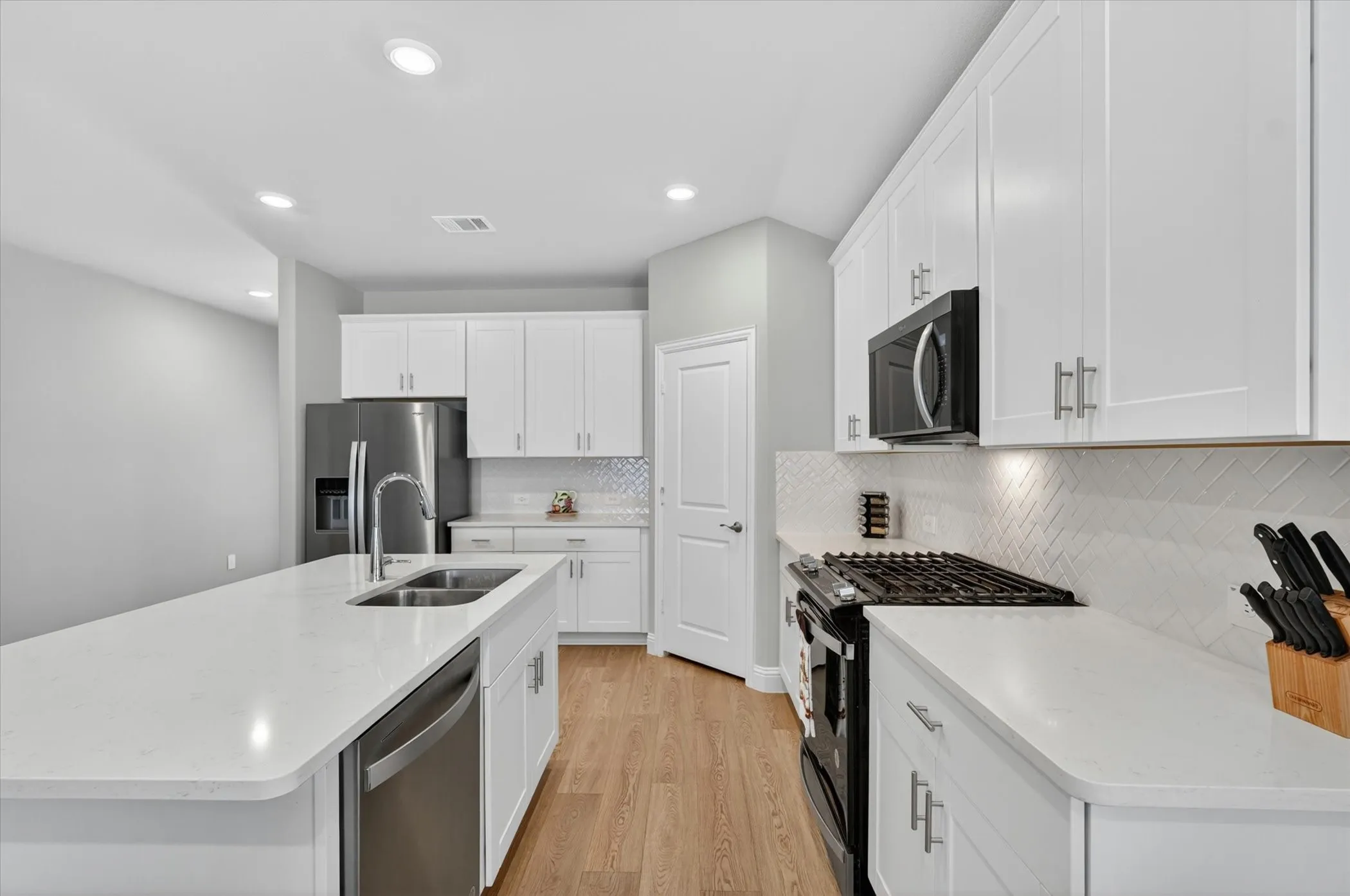 Modern kitchen featuring a large island with an undermount sink, white shaker cabinetry, stainless steel appliances, and wood-finish flooring