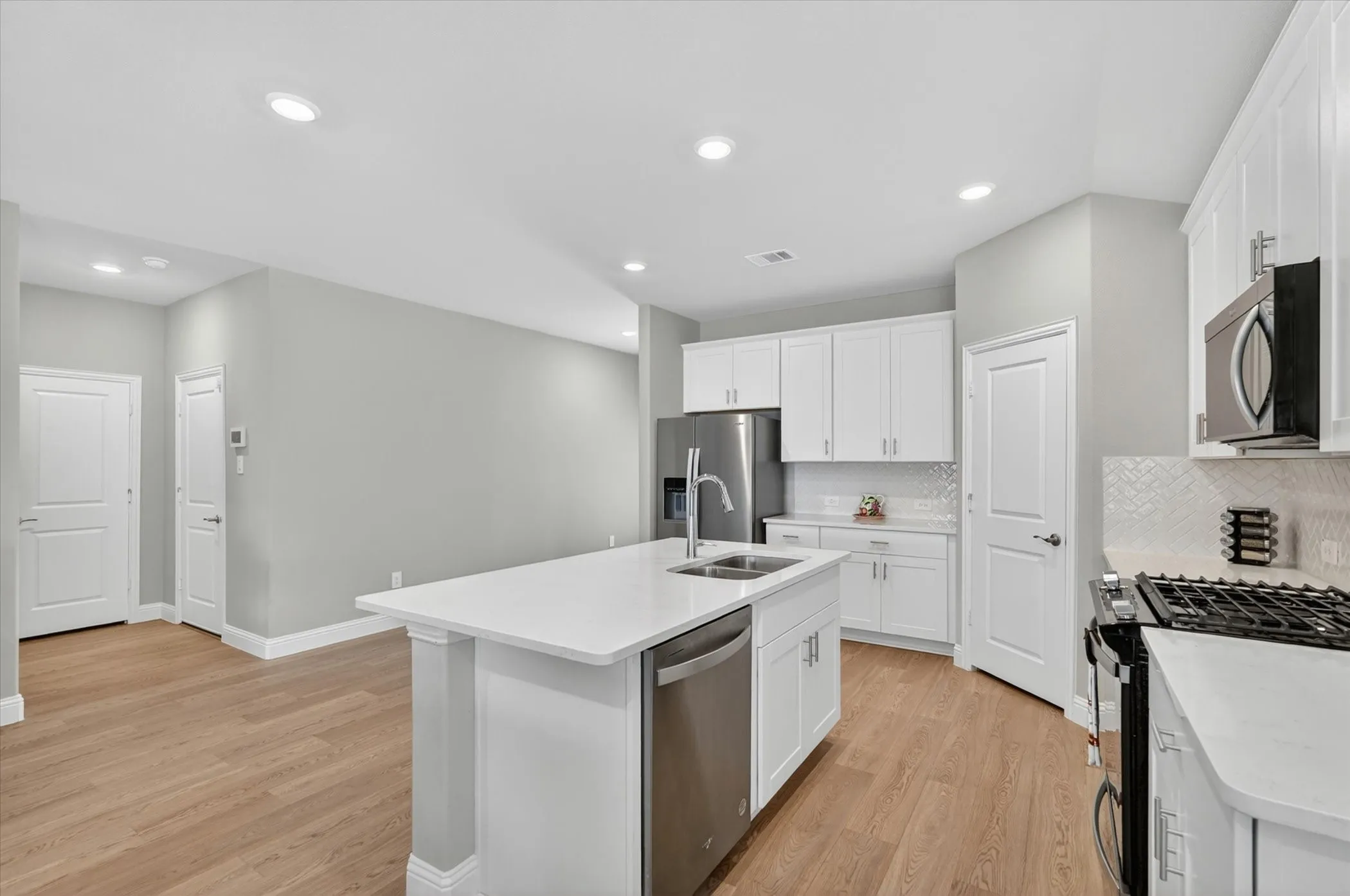 Kitchen featuring a central island with an undermount sink, stainless steel appliances, white cabinetry, light countertops, and wood-finish flooring