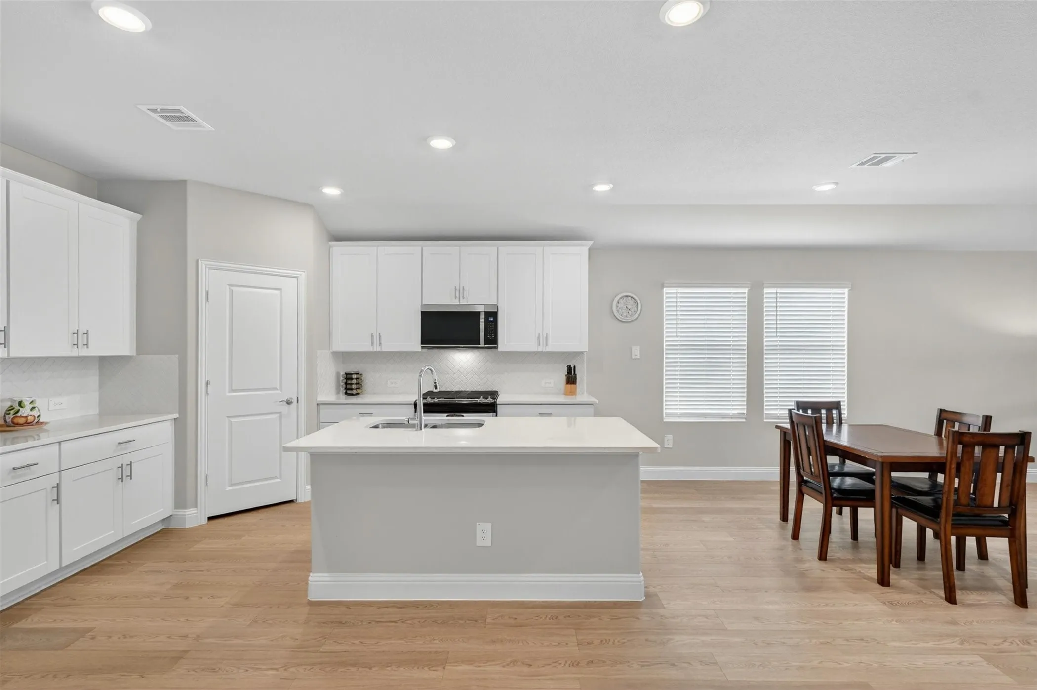 Kitchen featuring white cabinetry, light-toned countertops, a central island with a sink, stainless steel appliances, and wood-finish flooring