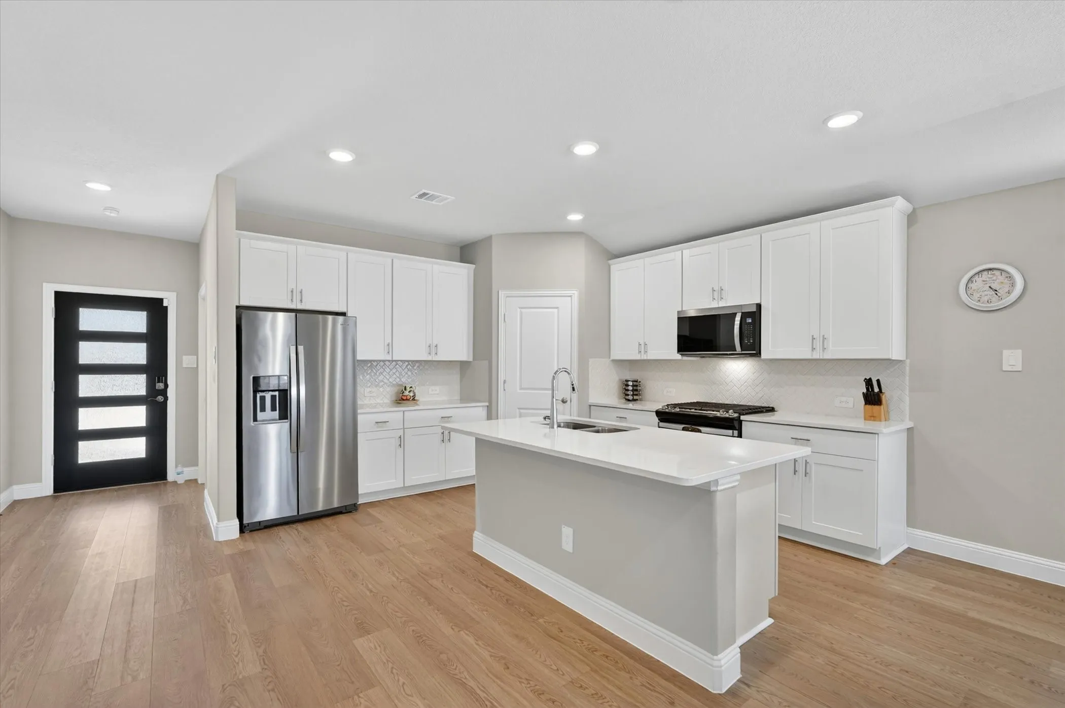 Open-concept kitchen with a central island, white shaker cabinetry, stainless steel appliances, and wood-finish flooring
