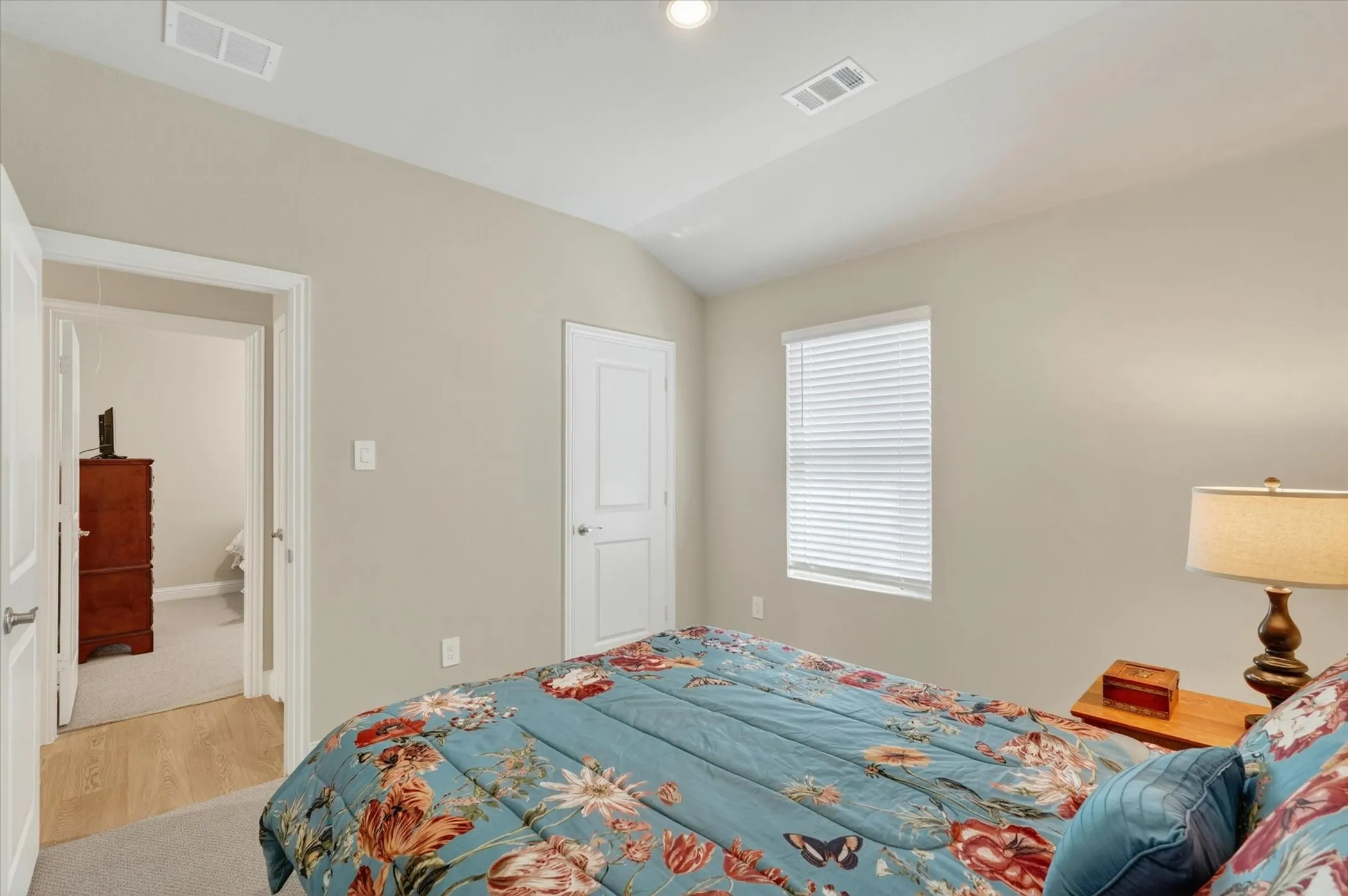 Bedroom with vaulted ceiling, light beige wall paint, single window with horizontal blinds, and a white two-panel interior door