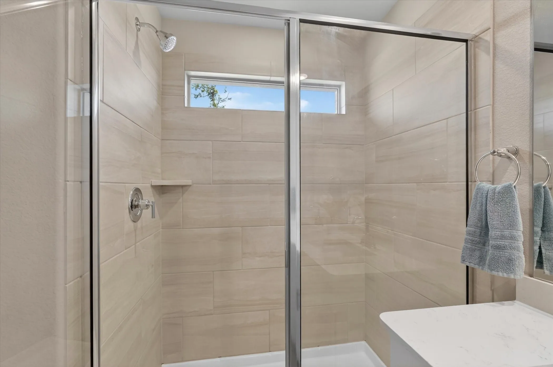 Glass-enclosed shower with full-height tiled walls, an integrated shelf, and a transom window