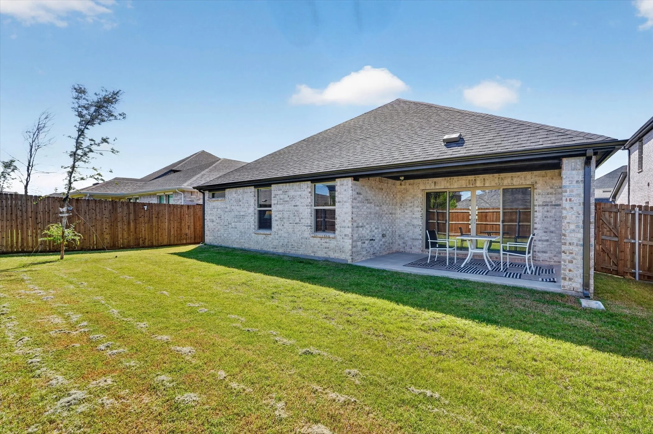 Expansive backyard featuring a covered patio, sliding glass door access, white brick exterior, and a wood privacy fence